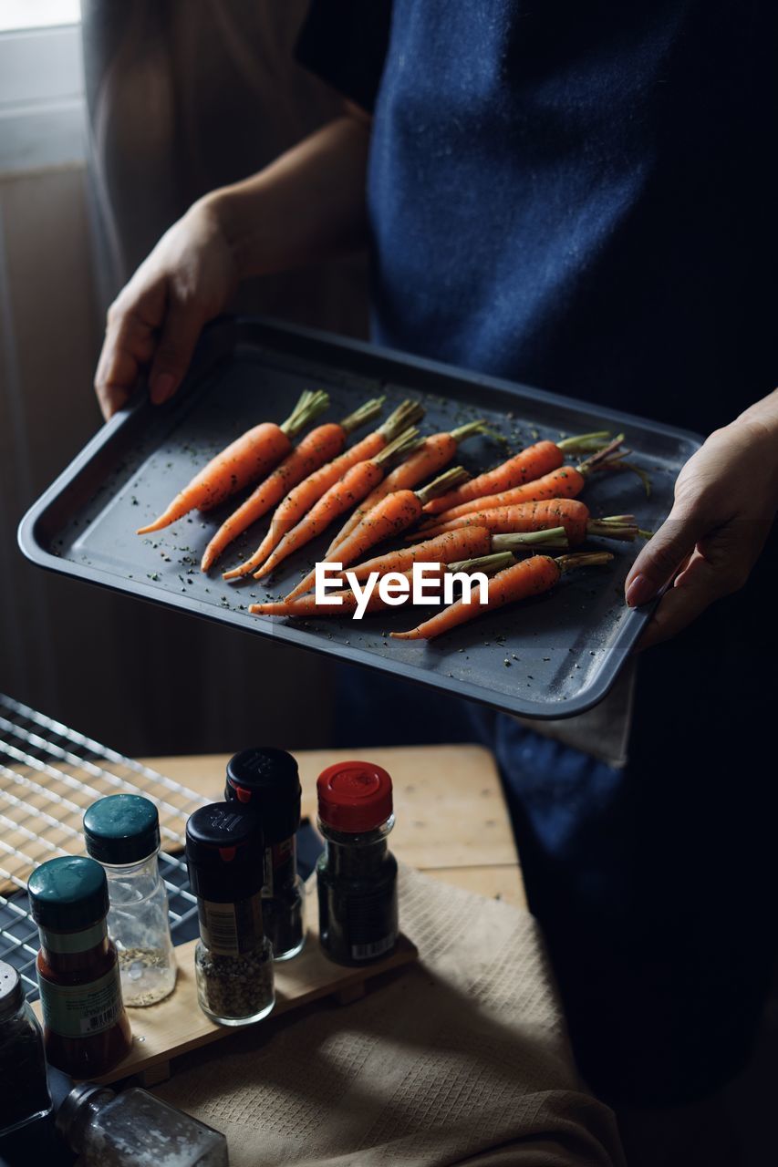 Midsection of woman holding carrots in tray at home