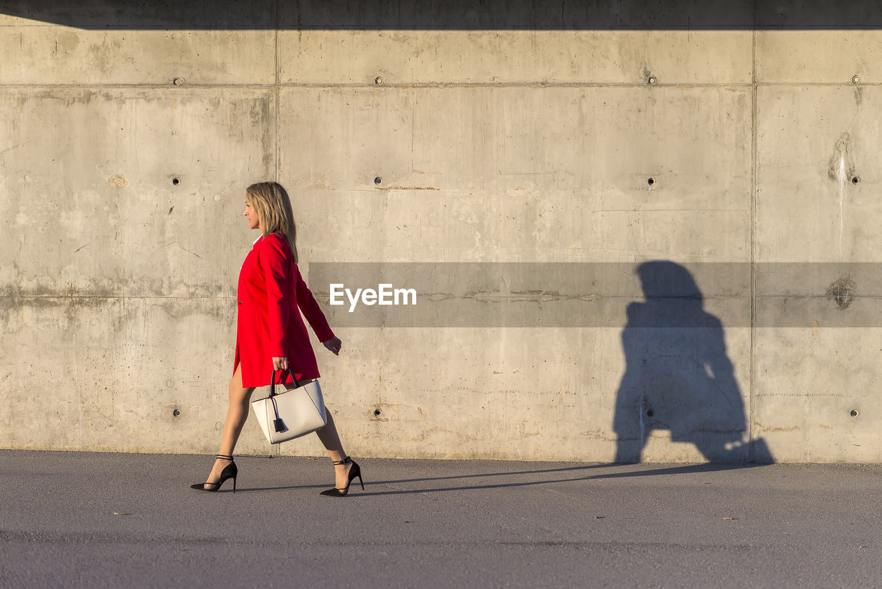 Side view of woman walking on footpath against wall