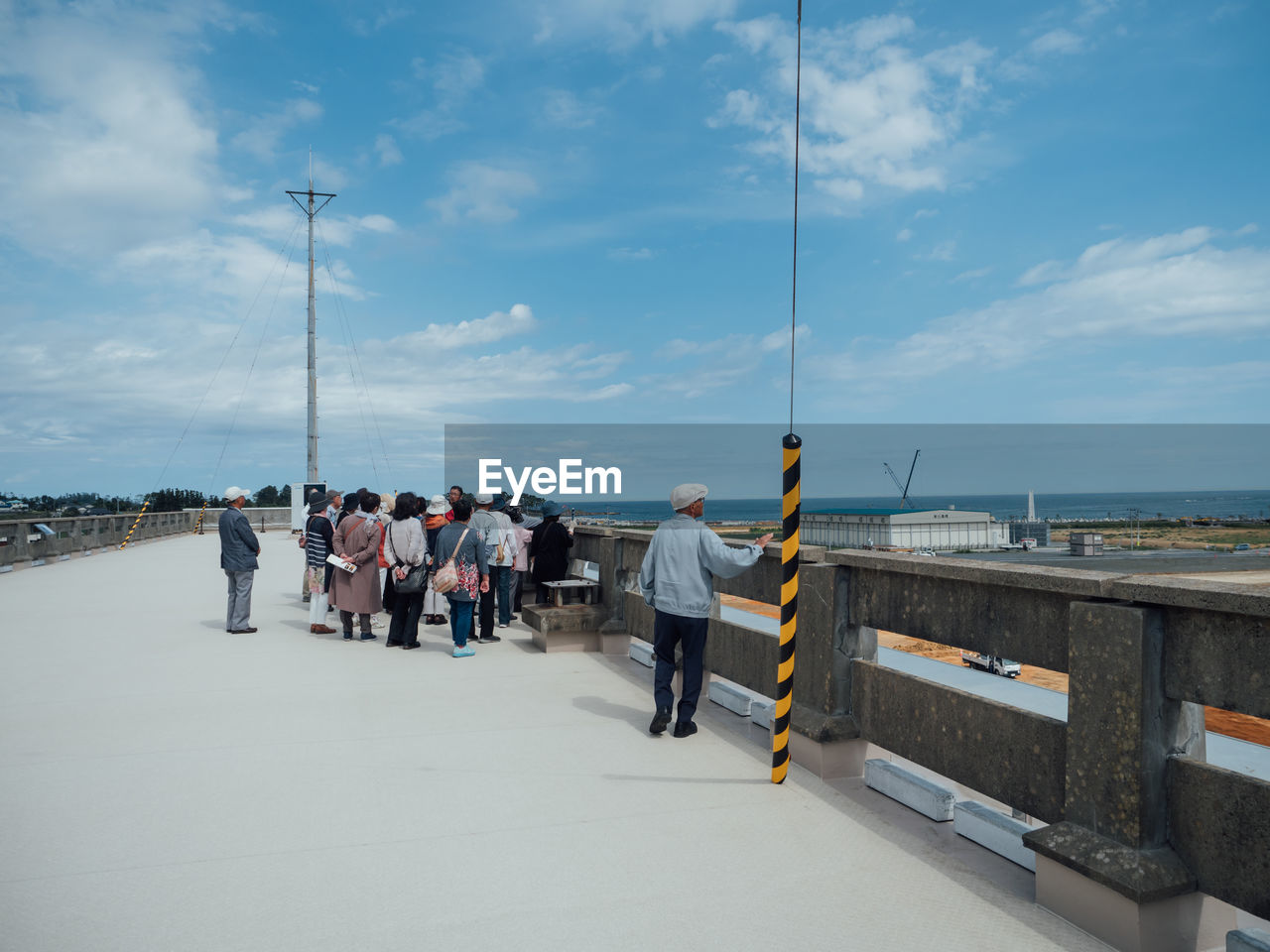 REAR VIEW OF PEOPLE WALKING ON STREET AGAINST SEA