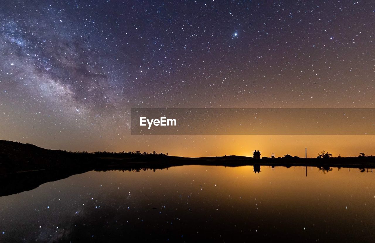 REFLECTION OF SILHOUETTE TREES IN LAKE AGAINST SKY AT NIGHT