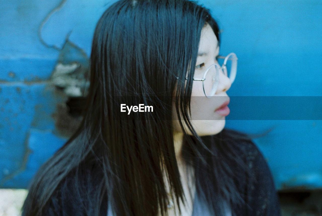 Close-up of young woman looking away sitting against wall