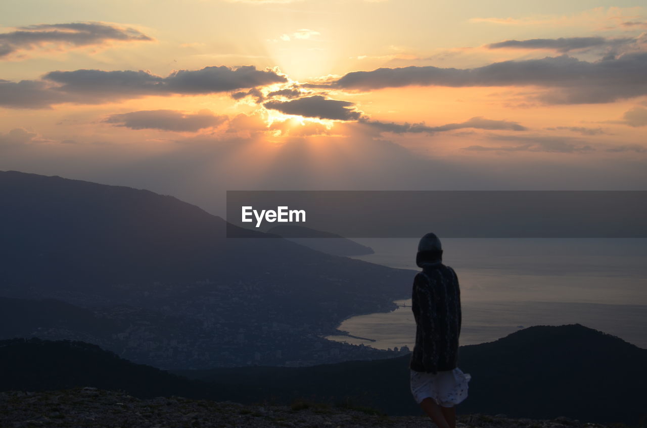 Rear view of woman  standing on mountain against sunset sky