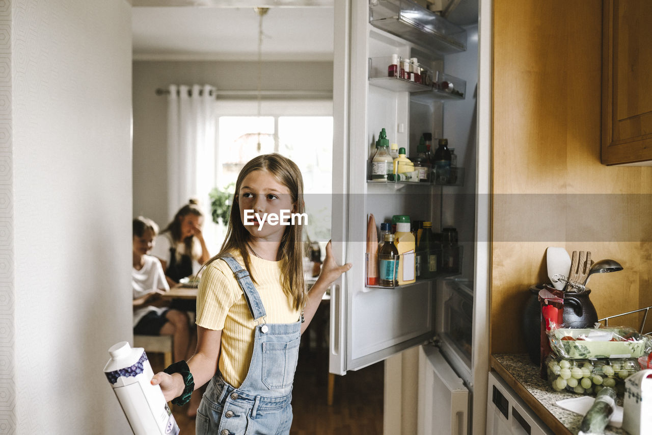 Caucasian girl with juice pack standing by refrigerator