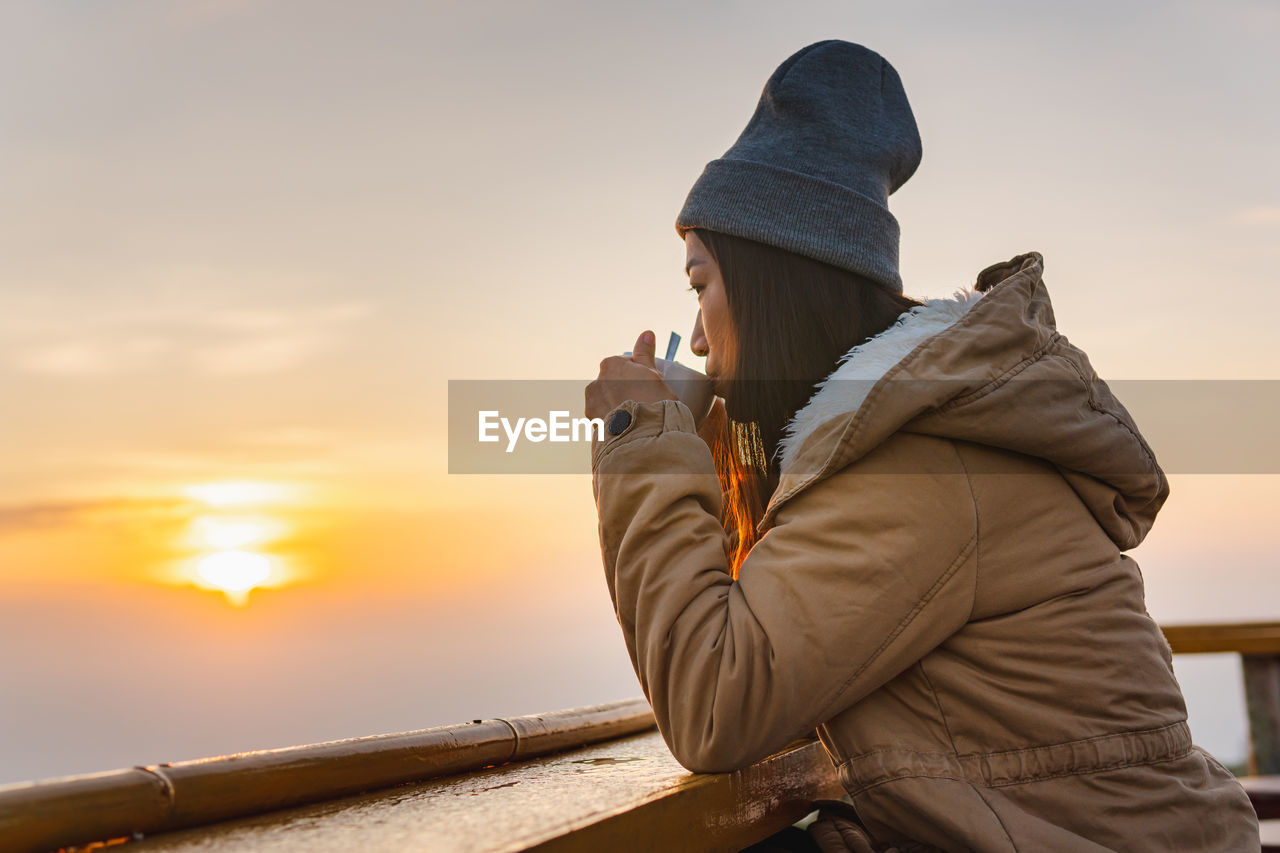 MIDSECTION OF WOMAN HOLDING SMART PHONE DURING SUNSET