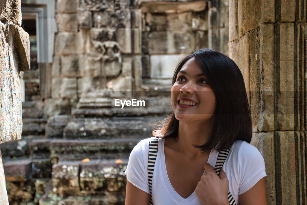 PORTRAIT OF SMILING YOUNG WOMAN AGAINST BUILDING