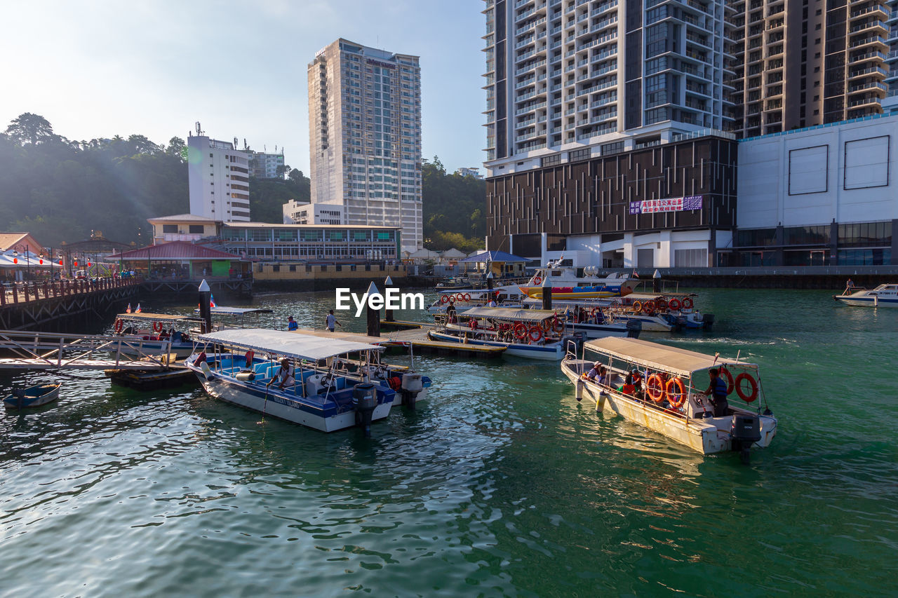 BOATS MOORED IN RIVER BY BUILDINGS IN CITY AGAINST SKY