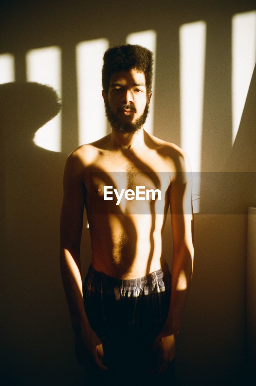 PORTRAIT OF SHIRTLESS MAN STANDING IN SUNLIGHT