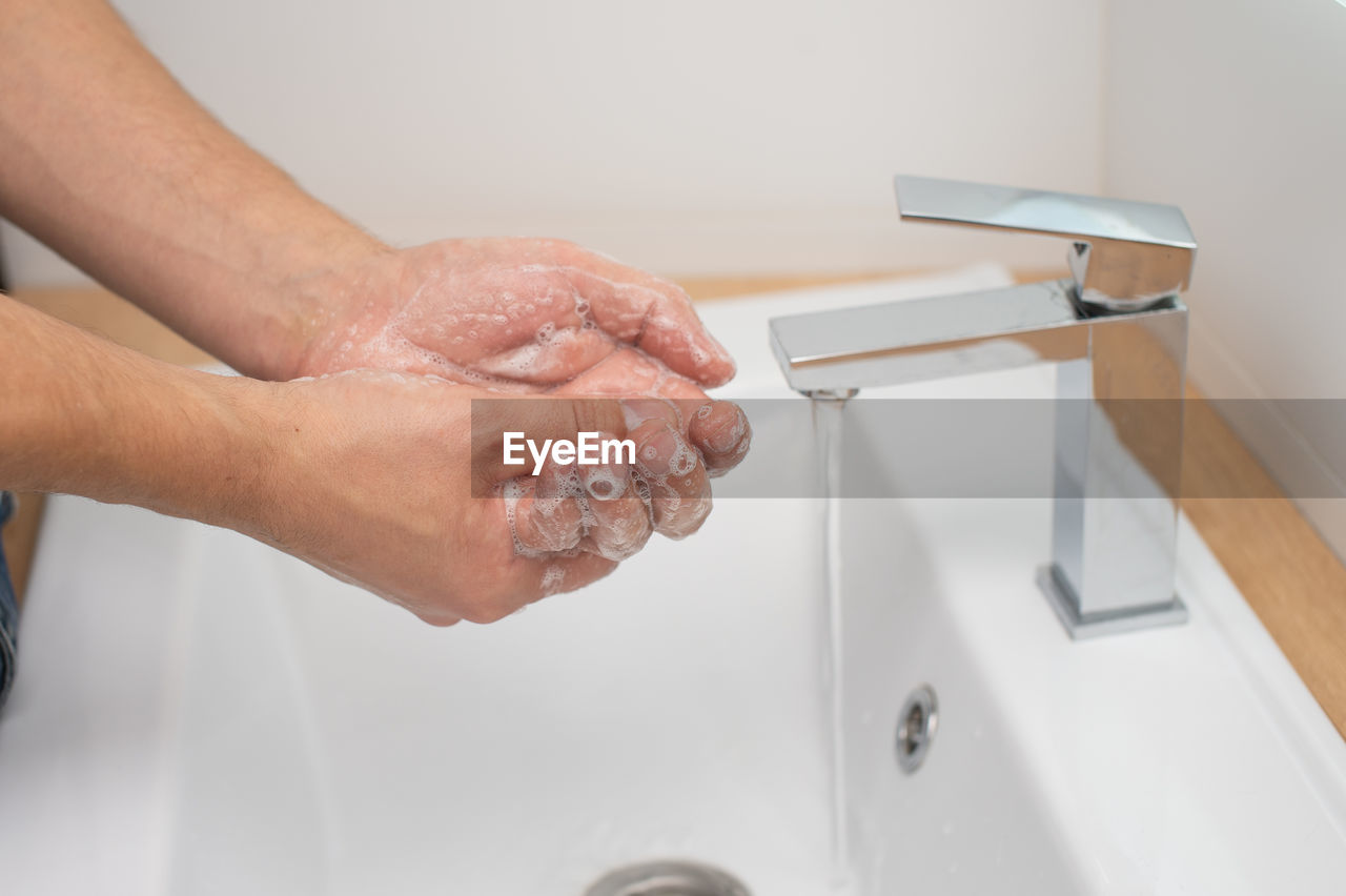 Men's hands with soap under a stream of water in the washbasin