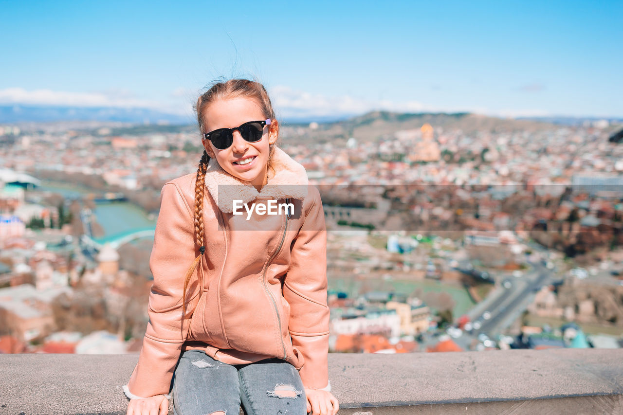 PORTRAIT OF SMILING YOUNG WOMAN IN CITY