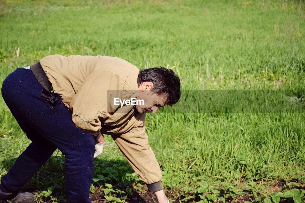 one person, grass, men, lawn, plant, agriculture, nature, adult, full length, green, land, bending, field, casual clothing, lifestyles, day, outdoors, growth, meadow, soil, emotion, gardening