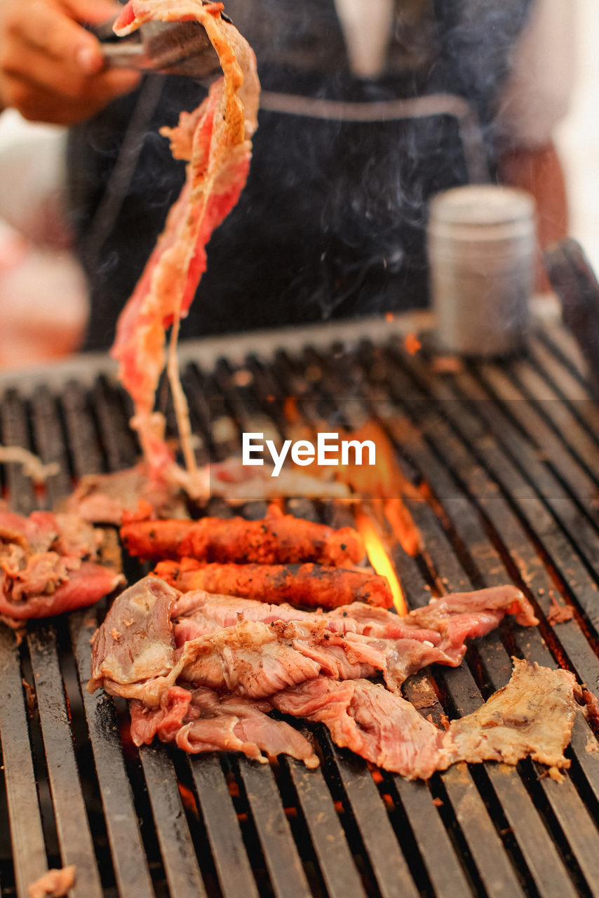 Cropped hand of person preparing meat on barbecue grill