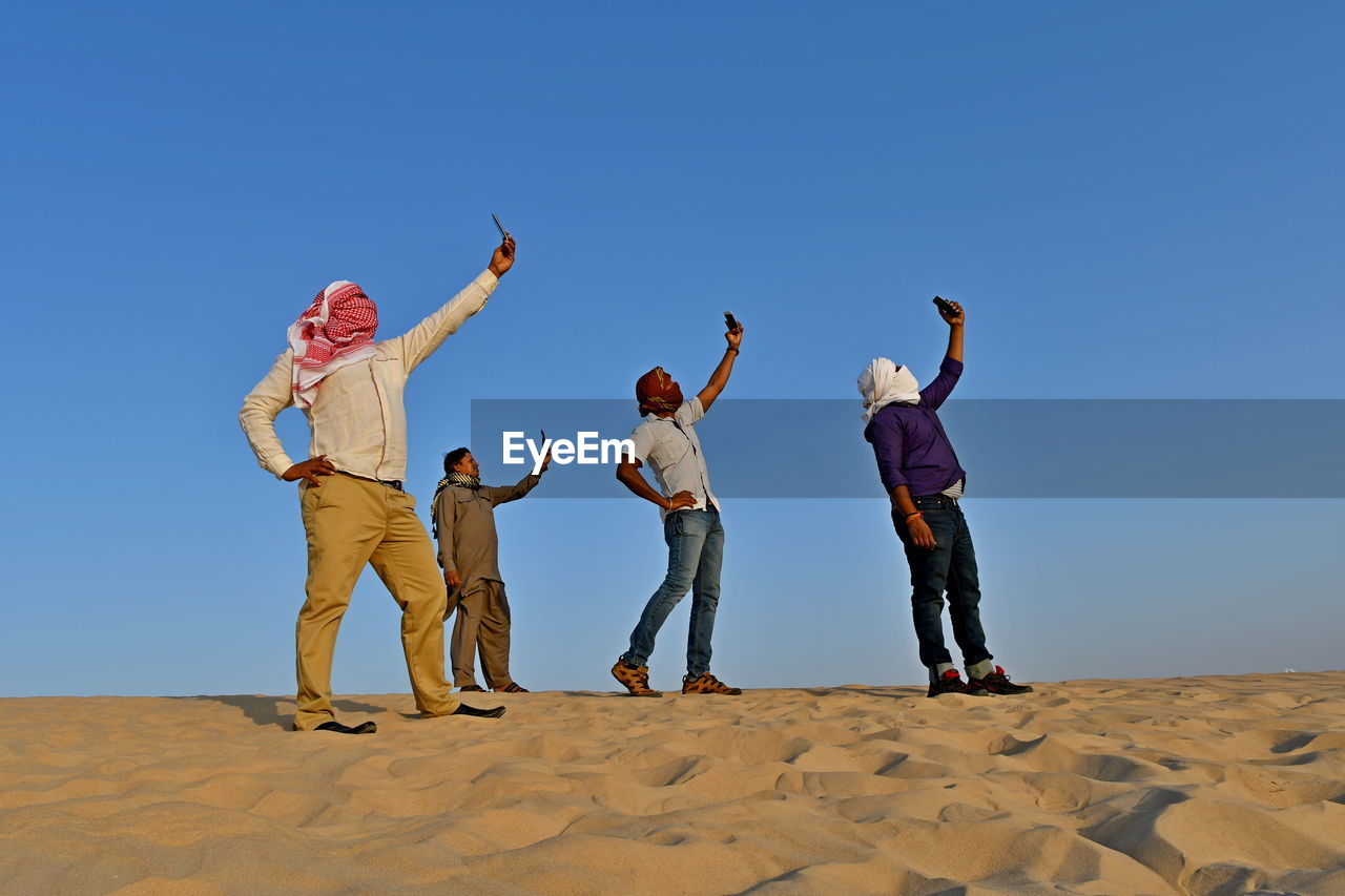 Men with covered face taking selfie while standing on sand at beach