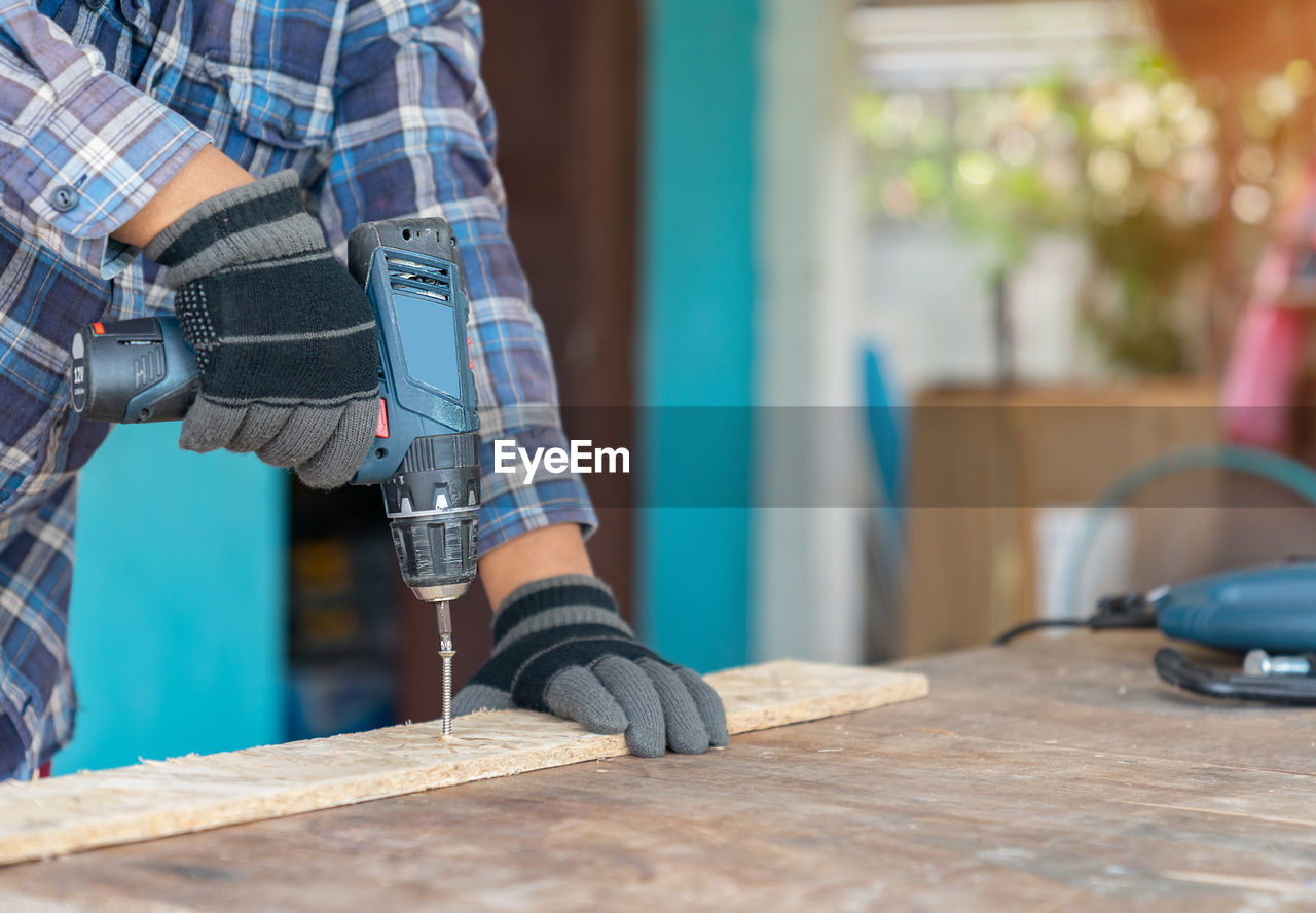 Carpenter use cordless screwdriver to driving screw nail into wood sheet on the table in workshop