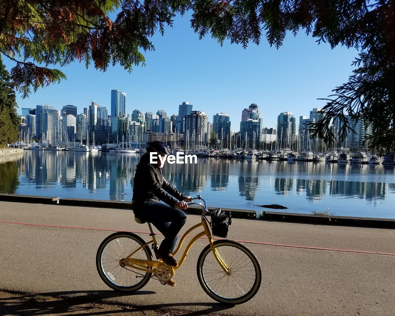 MAN RIDING BICYCLE BY RIVER AGAINST CITY