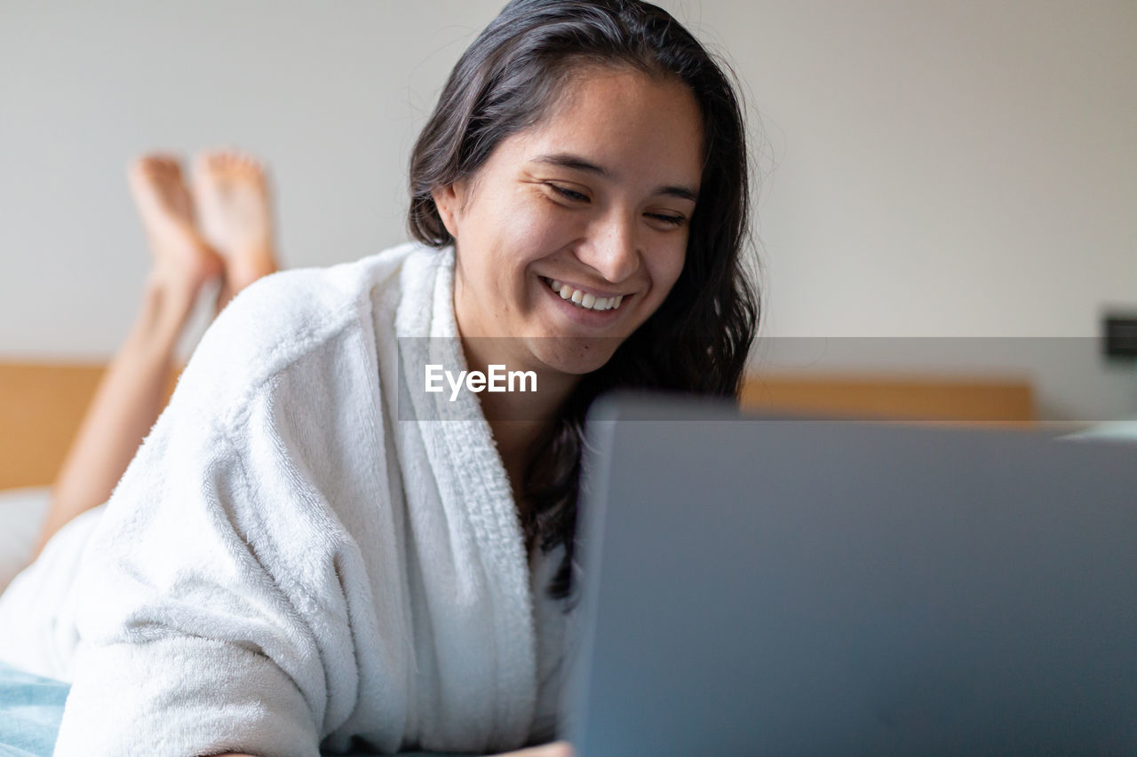 Happy woman surfing internet on laptop in bedroom at home