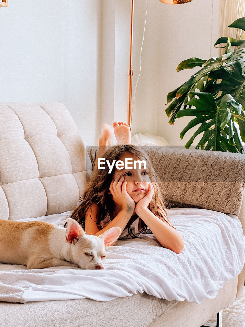 Portrait of young girl sitting on sofa at home with her dog watching television 