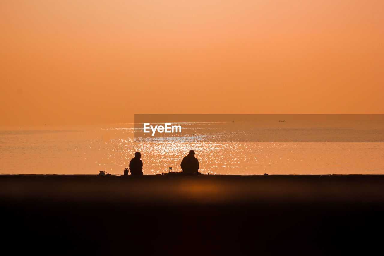 Silhouette people on sea against sky during sunset