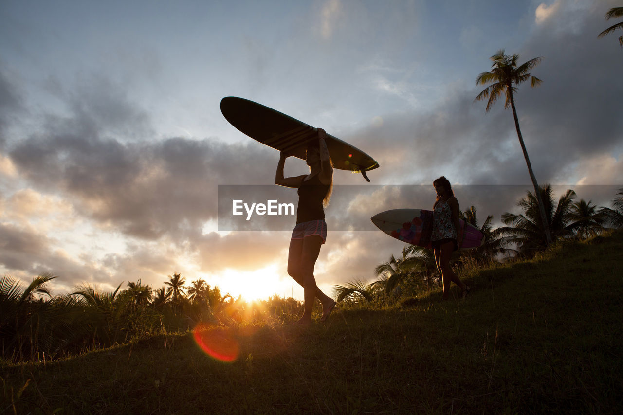 Two women carrying surfboards on a hill during sunset on siargao island, philippines