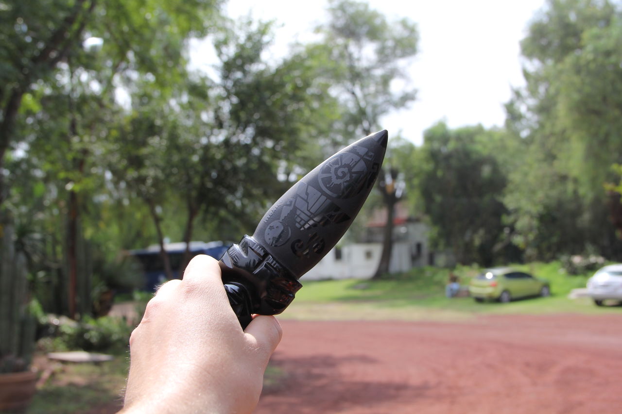 Cropped image of hand holding toy against trees outdoors