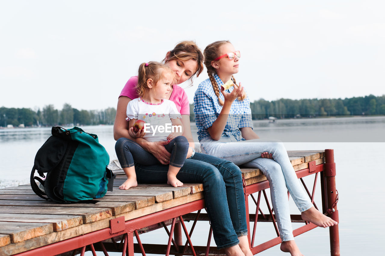 Mother with daughters sitting on pier over lake