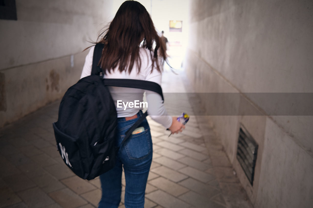 REAR VIEW OF WOMAN WITH UMBRELLA WALKING ON FOOTPATH