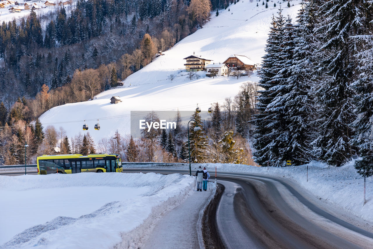 Snow covered road, mountains, trees and yellow ski bus at ski region schladming dachstein, austria