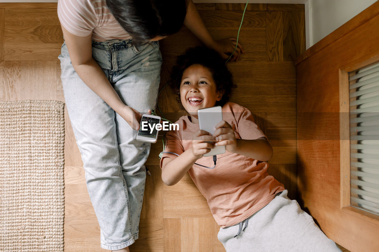 Directly above shot of happy siblings using smart phones on hardwood floor at home