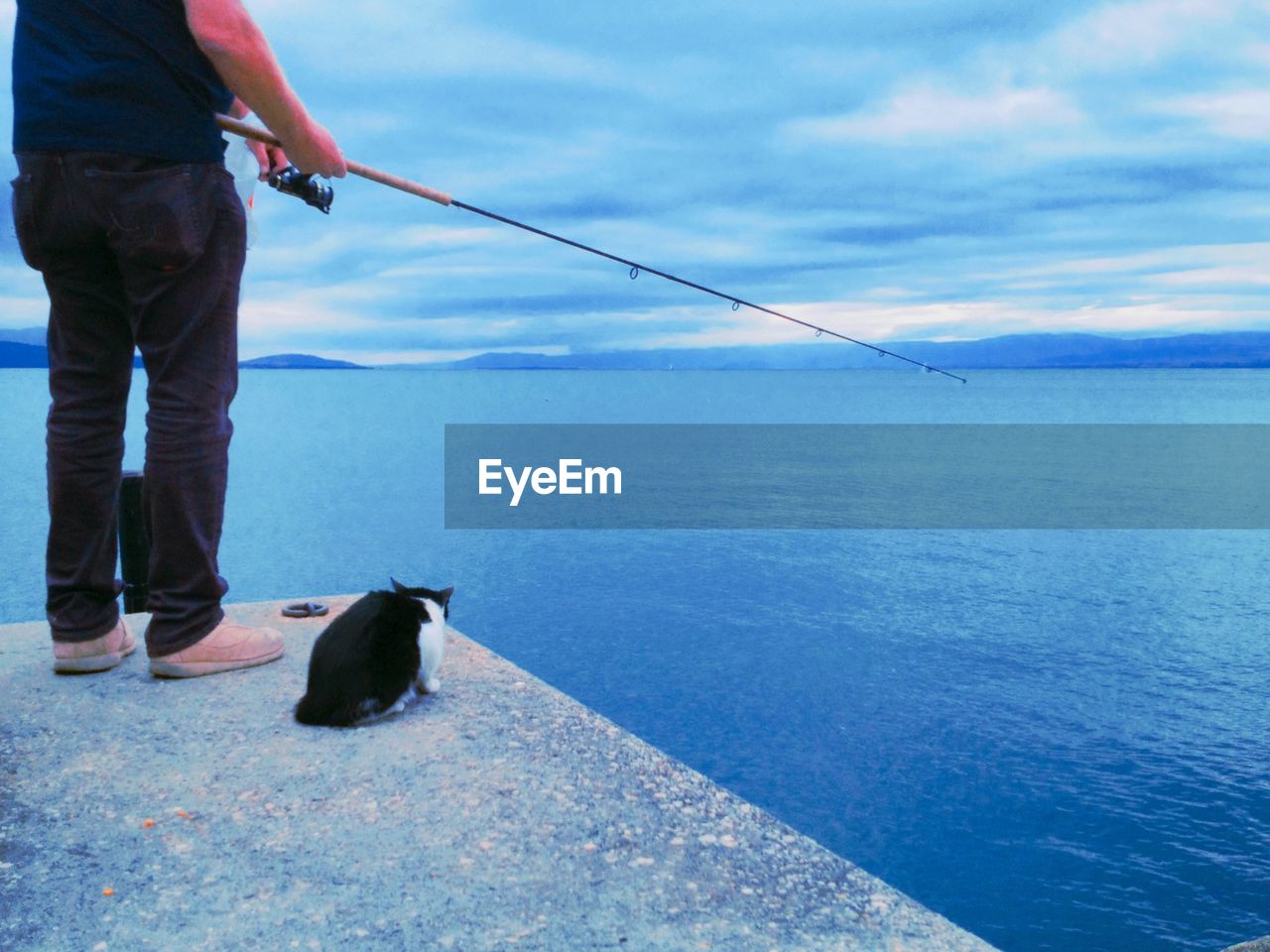 Man fishing on sea against sky with a cat