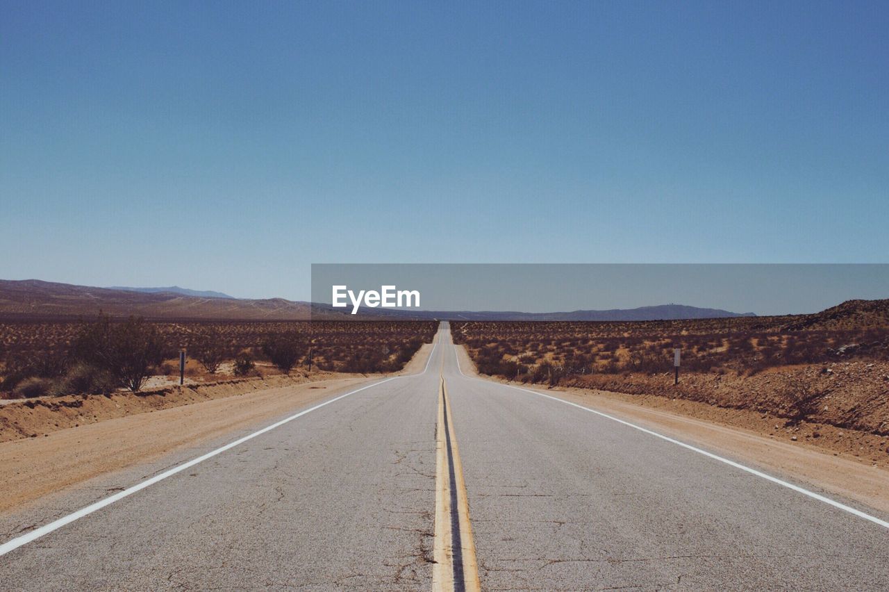 Empty road along landscape against clear sky