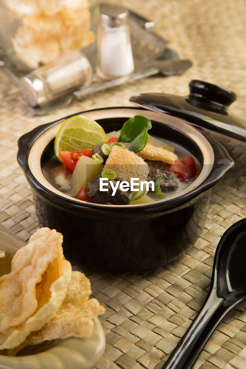 Tripe broth in porcelain pot placed on woven wicker mat