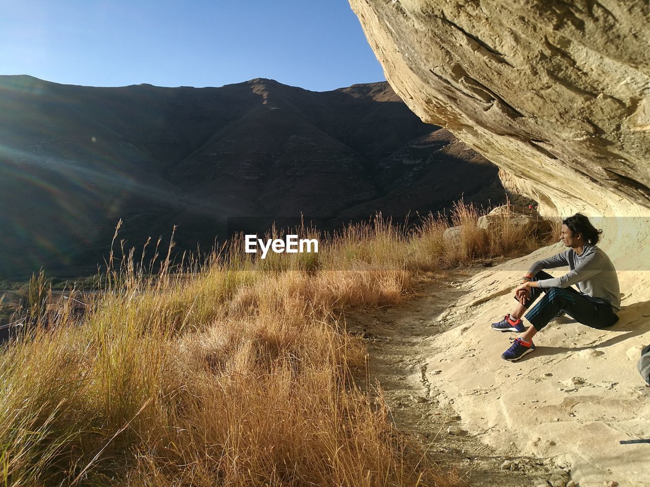 Full length of man sitting by rock formation on cliff against mountain