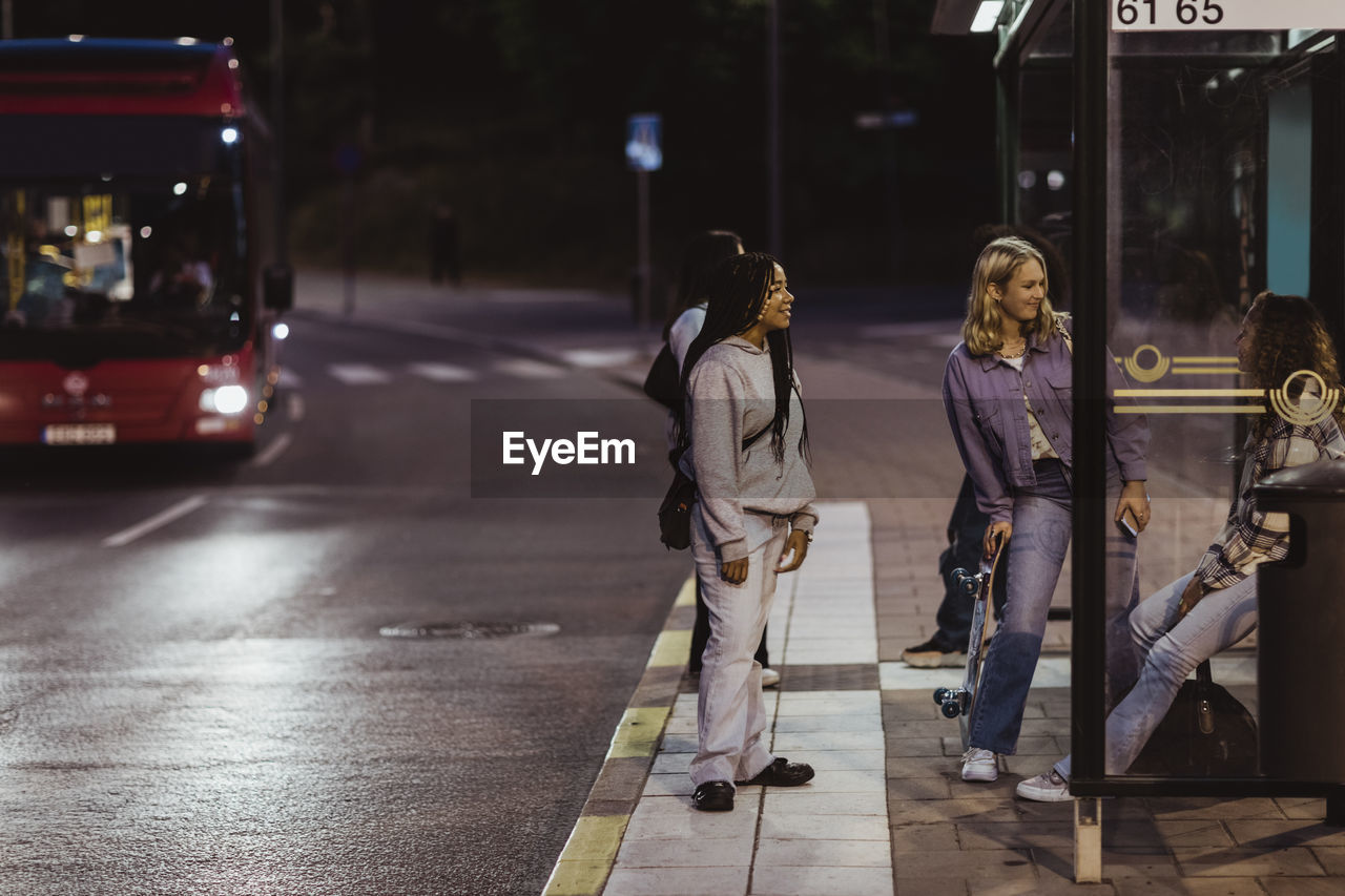 Female friends sitting on bus stop at night