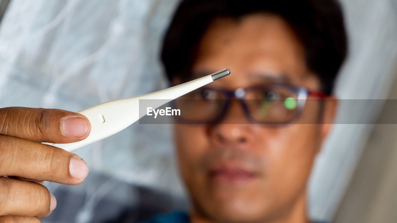 Close-up of man holding thermometer