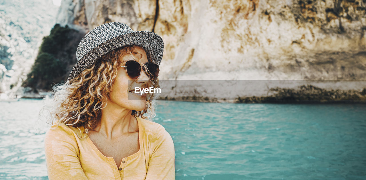 portrait of young woman wearing sunglasses while standing against lake