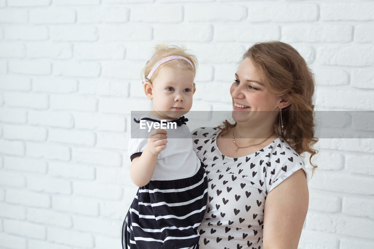 portrait of smiling young woman standing against wall at home