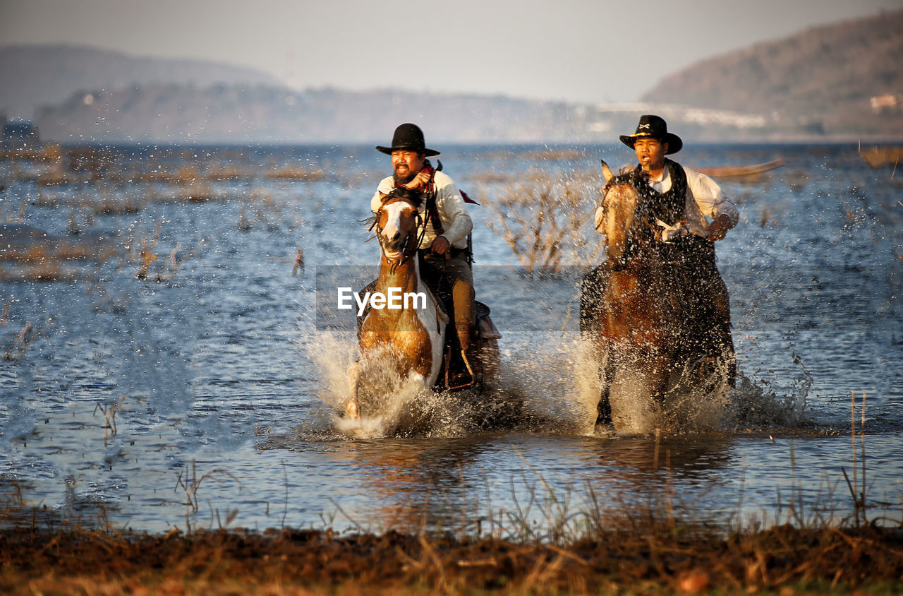 Men wearing costumes riding horses in lake against sky