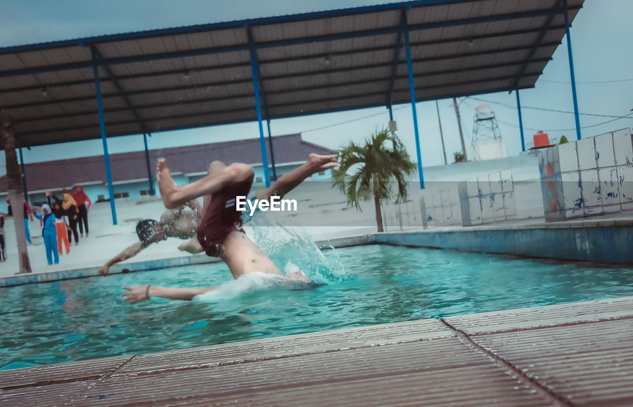 PEOPLE JUMPING IN SWIMMING POOL AT RESORT