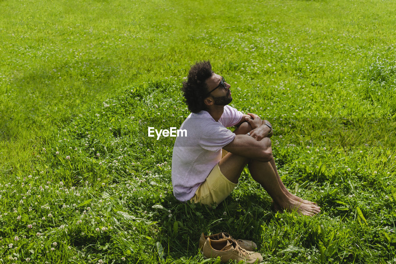 Man hugging knees sitting on grass in park