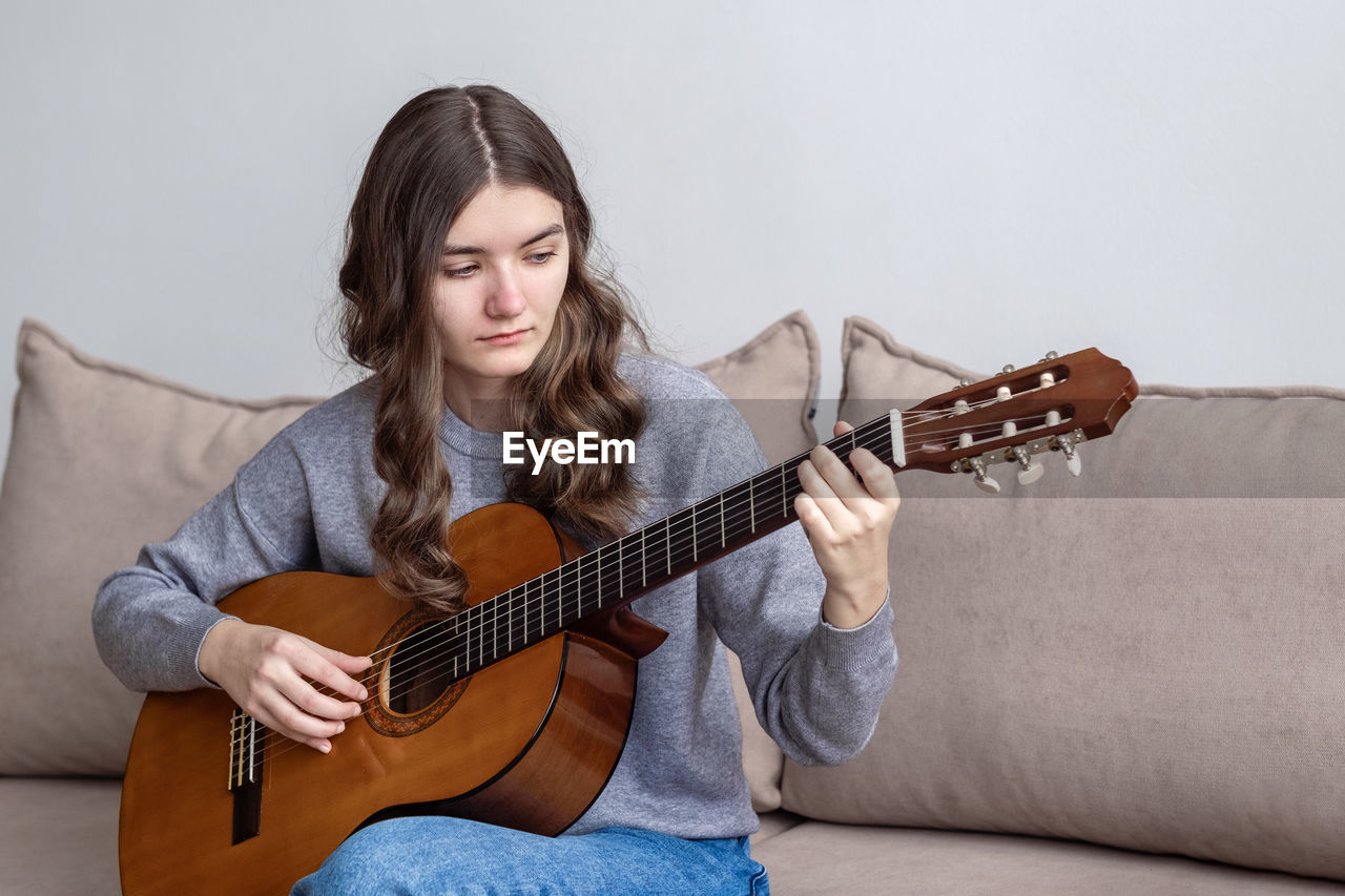 Girl playing guitar on sofa at home