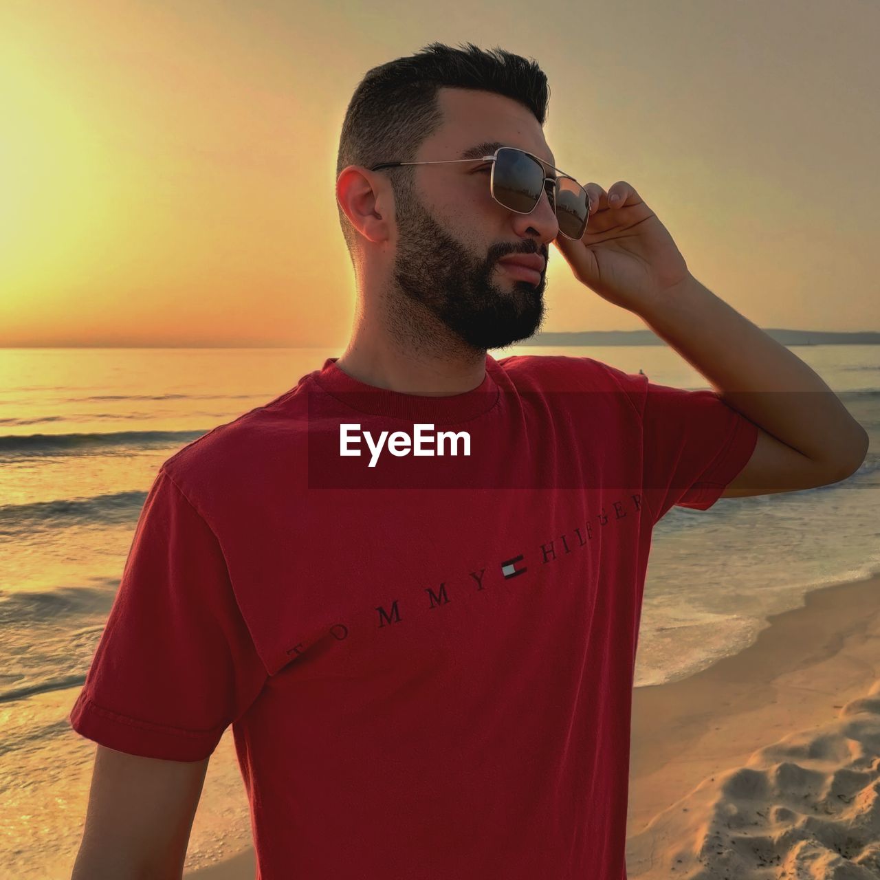 sea, water, beach, one person, sunset, red, land, sky, adult, nature, young adult, waist up, men, leisure activity, standing, fashion, sand, vacation, glasses, holiday, sunglasses, casual clothing, beard, sunlight, trip, person, summer, lifestyles, beauty in nature, facial hair, horizon, relaxation, sun, horizon over water, looking, scenics - nature, t-shirt, outdoors, clothing, holding, travel destinations, portrait, travel, orange color