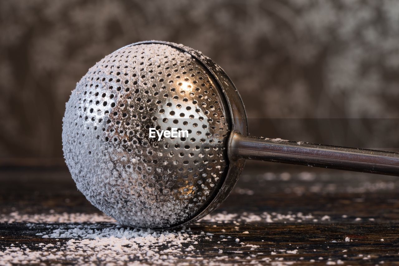 Close-up of sugar duster with powdered sugar on wooden table