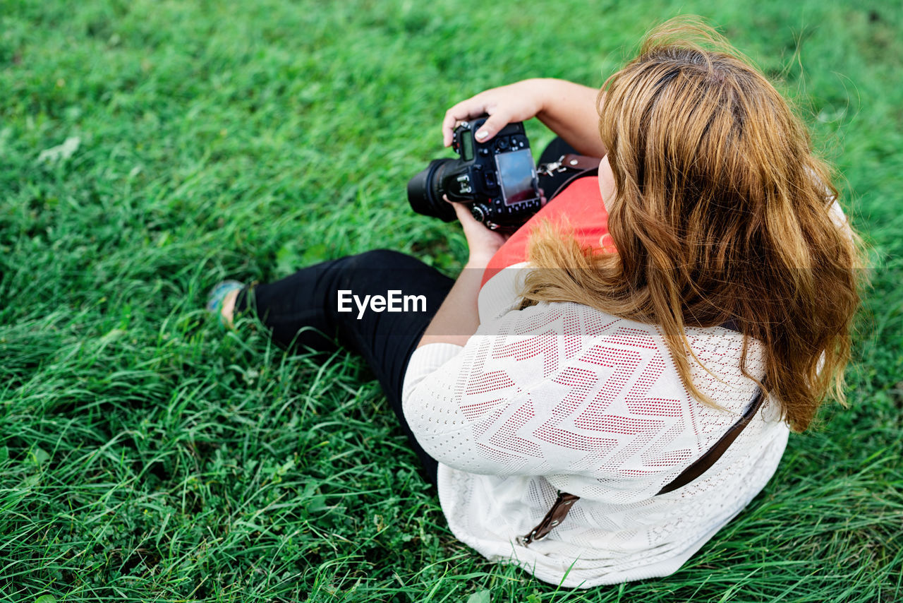 Young woman holding camera while sitting on grass outdoors