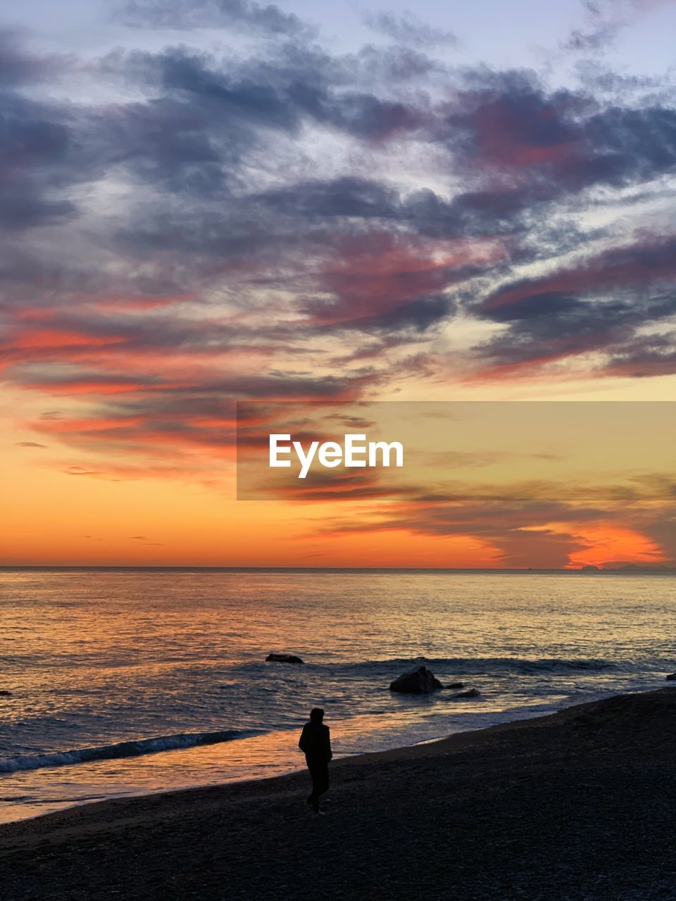 Walking alone on the beach, along the sea, admiring the sky and a spectacular sunset, orange colors 