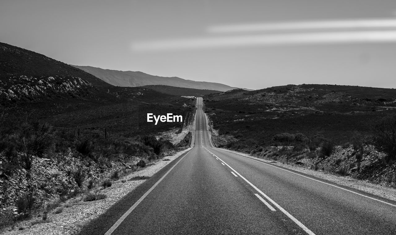 Empty road leading towards mountain against sky