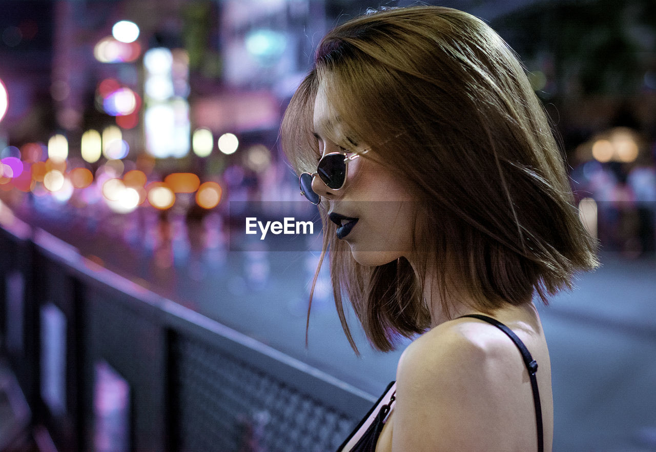 Young woman wearing sunglasses in city at night