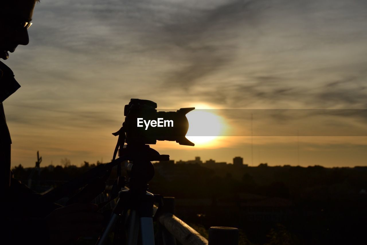 Man with digital camera against sky at dusk