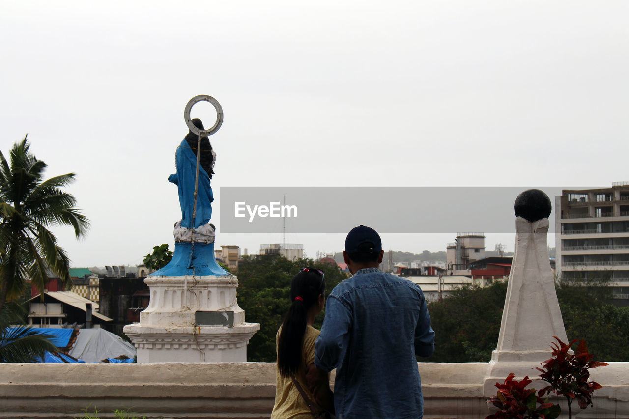 REAR VIEW OF MAN STATUE AGAINST SKY