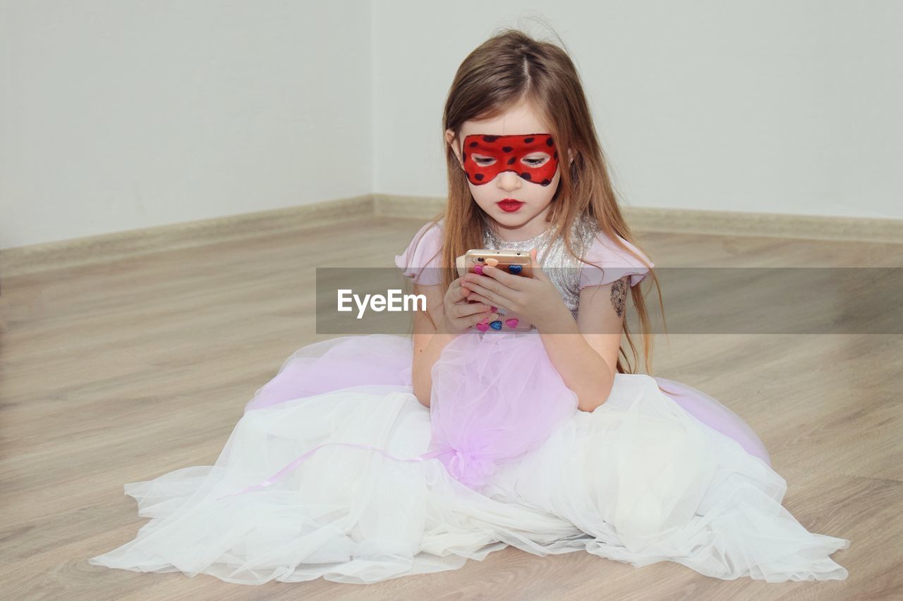 Girl wearing dress while using phone on hardwood floor