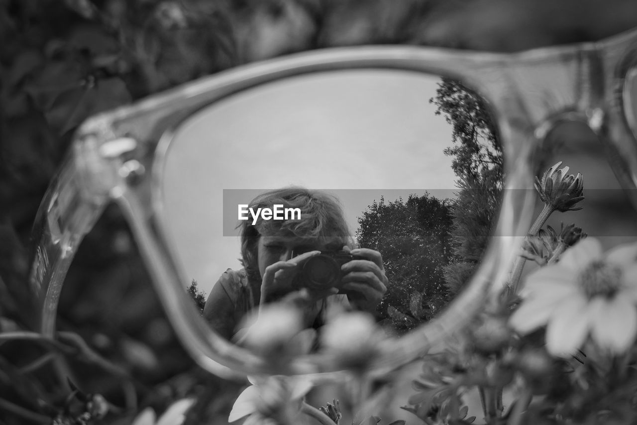 Reflection of woman photographing through camera in sunglasses on grass