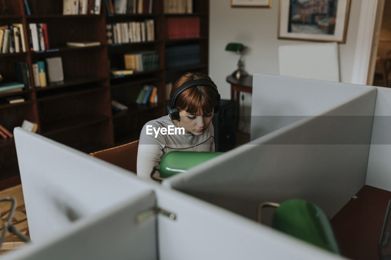 Teenage girl wearing wireless headphones while sitting in library